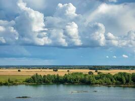 Amazing landscape with large white cumulus clouds over the lake and plain. Summer landscape on the banks of the green river at sunset. photo