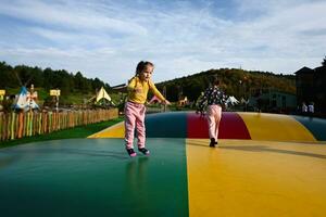 Little girl jumping on a trampoline in an amusement park. photo