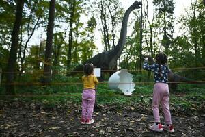 Little girls taking a picture of a dinosaur in a park. photo