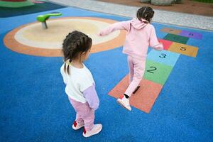 Back view of two girls playing hopscotch game at playground photo