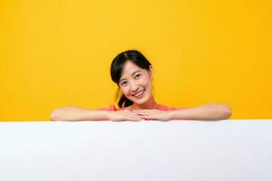 young asian sports fitness woman happy smile wearing pink sportswear standing behind the white blank banner or empty space advertisement board against yellow background. wellbeing lifestyle concept. photo