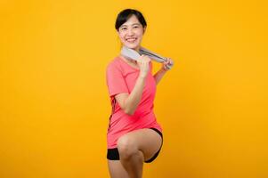 Portrait young asian sports fitness woman happy smile wearing pink sportswear and face towel doing exercise training workout against yellow studio background. wellbeing and healthy lifestyle concept. photo