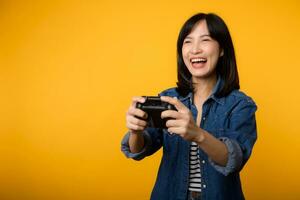 Portrait young asian woman with happy success smile wearing denim clothes holding joystick controller and playing video game. Fun and relax hobby entertainment lifestyle concept. photo