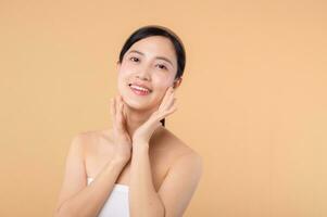 Beautiful girl asian model touching fresh glowing hydrated facial skin on beige background closeup. Beauty face young woman with natural makeup and healthy skin portrait. Skin care concept photo