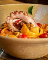 tagliatelle con pulpo, tomate y cebolla en un cuenco foto