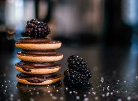 Chocolate macaroons with blackberries on a black background. photo