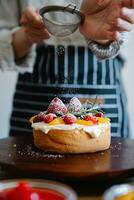 Chef sprinkling icing sugar on a fresh fruit tart with berries photo