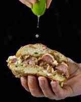 Sandwich with bacon, onion and cheese in hand on a black background photo