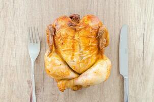 whole roasted chicken with knife and fork on wooden table, top view photo