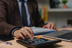 Businessman working on laptop and accounting financial marketing report document investment paperwork. hands of accountant using calculator to calculate tax refund economy. photo