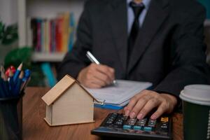 real estate agent with house. Business person holding pen sign a contract approved on mortgage loan contract agreement document house plan on the table. photo