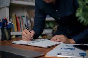 man hands with pen writing on notebook in the office.learning, education and work.writes goals, plans, make to do and wish list on desk. photo