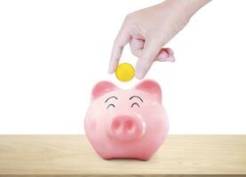 Hand picks up a gold coin and puts it in a piggy bank on a wooden table. white background photo