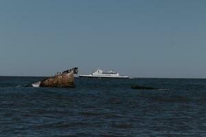 Image taken at Sunset beach in Cape May New Jersey. The sunken ship seen off the coast protruding from the water. The brown rusty hull looking weathered. Cape May Lewes ferry seen passing by. photo