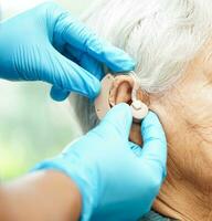 Asian senior woman patient using hearing aid in ear to reduce hearing loss problem. photo