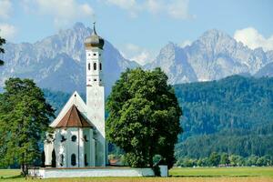 a white church in the middle of a field with mountains in the background photo