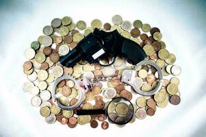 a gun, magnifying glass and handcuffs on a pile of coins photo