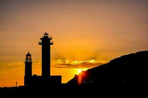 Silhouette of lighthouses and a hill with a sunset behind photo