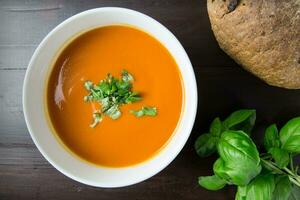 Tomato soup with basil and bread on wooden background. Top view. photo