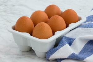 Fresh chicken eggs in a bowl on a white marble table with a blue napkin photo