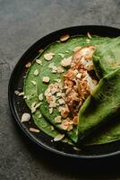 Spinach crepes with ice cream, nuts and honey on black plate photo