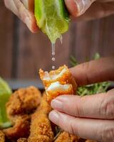 Close-up of a person's hand dipping lime in fried chicken nuggets photo