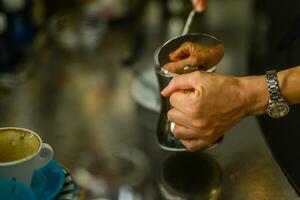 manos de joven mujer barista torrencial al vapor cremoso Leche en capuchino taza a el bar encimera. foto