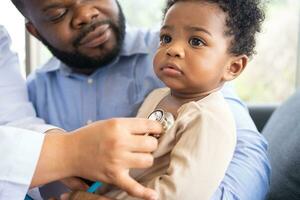 Pediatrics doctor with stethoscope for lungs or chest checkup for examining cute little girl in medical healthcare hospital or clinic. Doctor check Heart And Lungs for Smiling African American Baby. photo