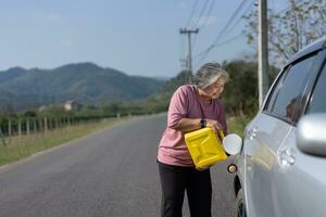 The car ran out of gas and stalled beside the road in suburbs and an elderly Asian woman used a gallon of spare gas to fuel the car. A woman prepares a gallon of spare gas to fuel before traveling. photo