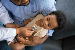 Pediatrics doctor with stethoscope for lungs or chest checkup for examining cute little girl in medical healthcare hospital or clinic. Doctor check Heart And Lungs for Smiling African American Baby. photo