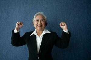 Portrait of middle aged business woman standing isolated on blue background and raise your arms to show success, looking at the camera with smile, Successful businesswoman, ceo, director, manager photo