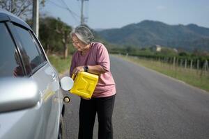 The car ran out of gas and stalled beside the road in suburbs and an elderly Asian woman used a gallon of spare gas to fuel the car. A woman prepares a gallon of spare gas to fuel before traveling. photo