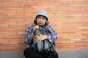 Poor tired stressed depressed elderly Asian woman homeless sitting on the street in the shadow of the building and begging for help and money, Elderly Asian woman abandoned concept photo