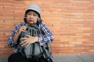 pobre cansado estresado Deprimido mayor asiático mujer Vagabundo sentado en el calle en el sombra de el edificio y mendicidad para ayuda y dinero, mayor asiático mujer abandonado concepto foto