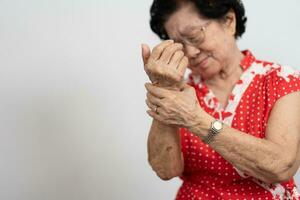 Elderly Asian woman patients suffer from numbing pain in hands from rheumatoid arthritis. Senior woman massage her hand with wrist pain. Concept of joint pain, rheumatoid arthritis, and hand problems. photo