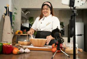 Young attractive Asian woman is blogging for her kitchen channel about homemade pizza while streaming online for webinar masterclass lesson. Vlogger broadcasting live video online teaching cooking photo