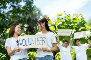 Happy young Asian students diverse volunteers hold a campaign sign for cleaning in the park, The concept of environmental conservation on world environment day, recycling, charity for sustainability. photo