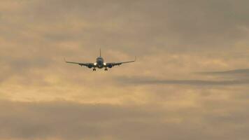 Slow motion footage of a jet plane approaching landing. Passenger airliner flies in the sunset sky, front view, long shot video