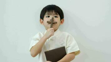 pequeño asiático chico reza participación un cruzar y un religioso libro, cristiano concepto, 4k resolución. video