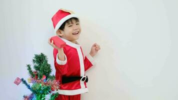 asiático chico vistiendo Papa Noel disfraz en pie y jugando cerca un divertido Navidad árbol. 4k resolución. video