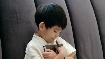 Little Asian boy prays holding a cross and a religious book, Christian concept, 4K resolution. video