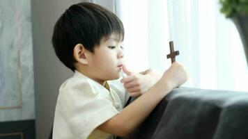 weinig Aziatisch jongen bidden met Holding de kruis, christen concept video