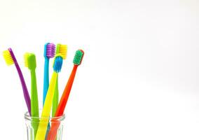 Tres cepillos de dientes - púrpura, naranja y amarillo con diferente de colores cerdas en un claro taza en un blanco antecedentes. aislado. vertical. foto en alto calidad.