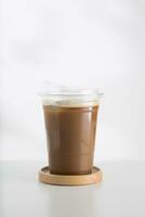 Iced cappuccino in a plastic glass on a white wooden table, minimalist-style picture. photo