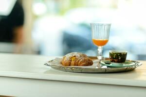 un bandeja con Café exprés café, naranja jugo y cuerno Panecillo en bar mostrador en el Mañana foto