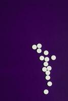 White pills over a solid violet background overhead shot. photo