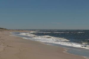 This beautiful beach image was taken at Cape May New Jersey. It shows the waves rippling into the shore and the pretty brown sand. The blue sky with the little bit of cloud coverage adds to this. photo