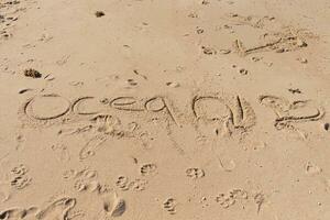 Beautiful brown sand with writing etched in. The word ocean can be seen written ion the beach. Footprints can be seen all around. photo