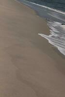 I loved the look of this beach scene as the waves crashed in. The pretty look of the whitecapped surf rushing in to the shore. The sand showing a different tone to where the water once was. photo