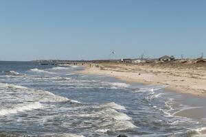 I loved the look of this beautiful beach scene. with pretty sand dunes. The water pummeling the shore with looks of rough seas. Whitecaps rippling through with pretty blue skies. photo